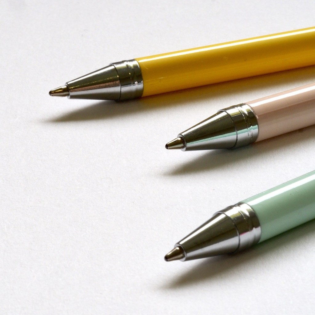 Three pens (yellow, light pink, light green) against a white background.